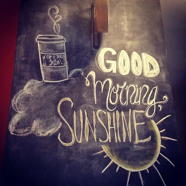 a chalkboard wall with a sketch of a coffee to-go mug that says, "cup of Joe" and a text that says, "good morning, sunshine".