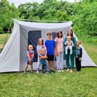 a family of 7 kids plus a mom standing outside of a canvas tent
