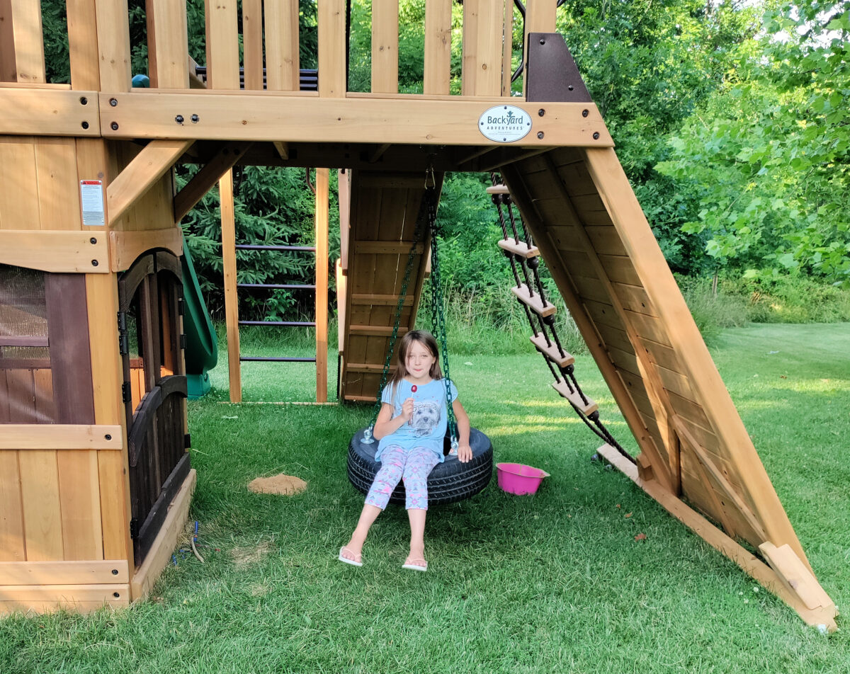 girl swinging on a tire swing on a custom designed Backyard Adventures playground